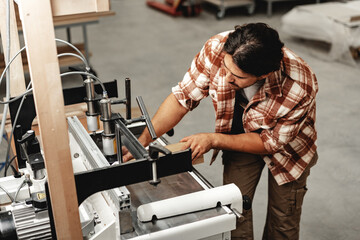 Wall Mural - Young carpenter operating machine for wood processing at a furniture factory