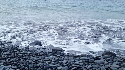 Wall Mural - Volcanic stones and sand are washed by the waves of the sea or ocean