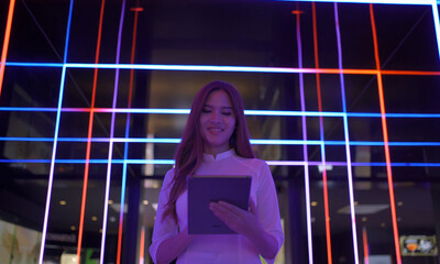 Portrait of Asian Vietnamese woman with Vietnam dress using a tablet device. Colorful neon stripes in night pub in Hanoi. People lifestyle.