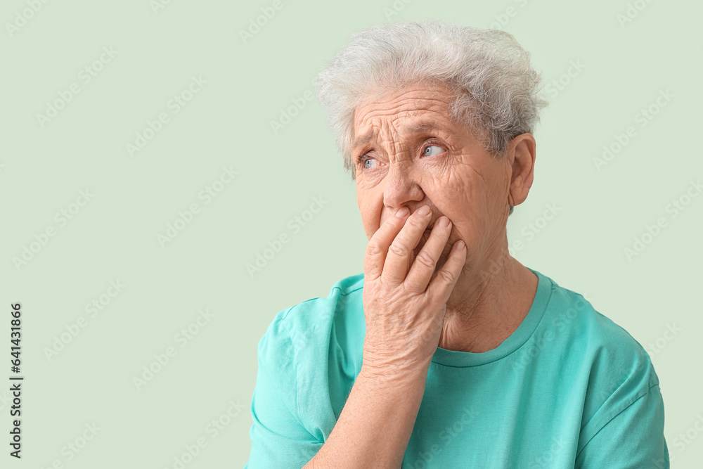 Upset senior woman on green background, closeup