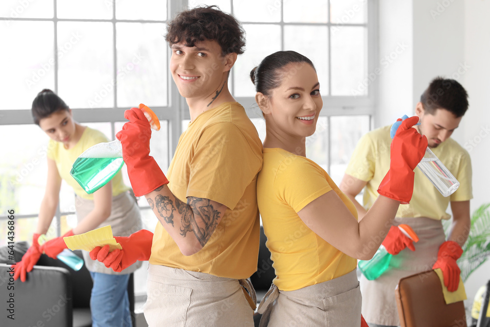Young janitors with bottles of detergent in office