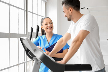 Wall Mural - Female physiotherapist working with young man on treadmill in rehabilitation center