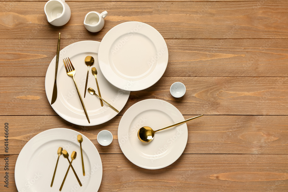 Clean plates, golden cutlery and pitchers on wooden table