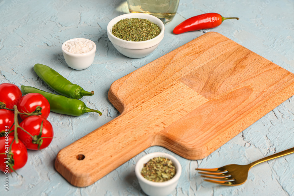Wooden cutting board, fresh vegetables and spices on color background