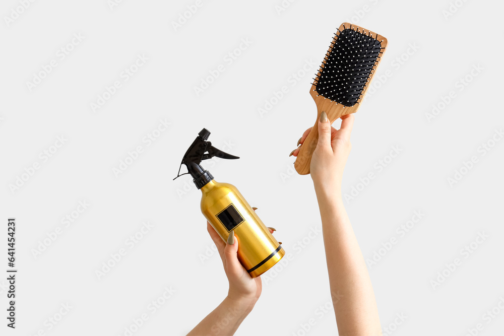 Female hands with hair spray and paddle brush on white background