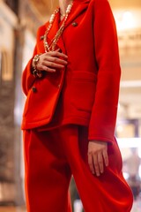 Wall Mural - Fashionable details of a gold chain hanging around the neck and a red classy jacket and pants. Fancy outfit, female accessories. Vertical