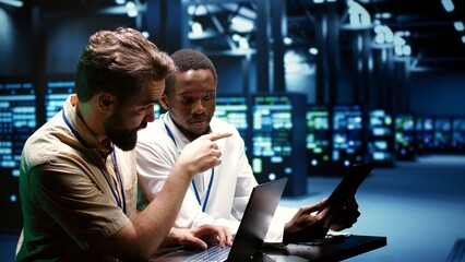 Colleagues running data center electronics diagnostic tests to determine and patch software issues. Mechanics using laptop and tablet to repair critical systems, checking for flaws