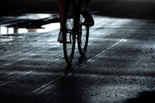 Unrecognizable Man Riding A Bike Down The Wet Road At Night, Puddles Illuminated By Moonlight  