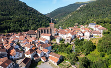 Scenic Aerial View Of Spanish Township Of Isaba With Brownish Tiled Roofs Of Residential Buildings And Medieval Fortified Church Of Saint Cyprian In Roncal Valley Surrounded By Green Pyrenees, Navarre