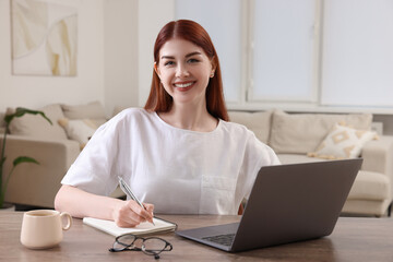 Poster - Happy woman with notebook and laptop at wooden table in room