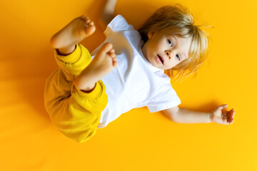 The kid is 2 years old with blonde hair, dressed in a white T-shirt and yellow pants on a yellow background. Emotions. The concept of childhood and family. Baby front view yellow isolated background