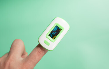 Pulse oximeter on finger showing oxygen saturation and heart rate. 