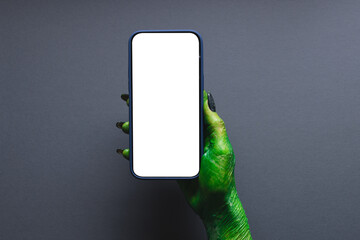 Wall Mural - Green monster hand holding smartphone with copy space on grey background