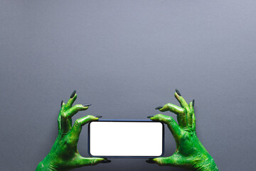 Wall Mural - Green monster hands holding smartphone with copy space on grey background