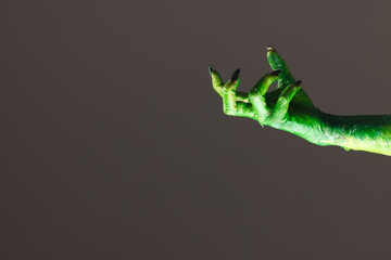 Wall Mural - Green monster hand with black nails reaching on grey background