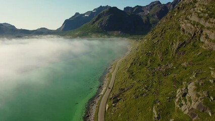 Wall Mural - View of a road in Lofoten in Summer, vanishing into the low fog and mist. Bright summer sun, mountains and turquoise sea. 4K resolution, 30 fps.