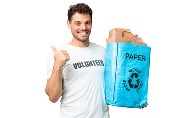 Poster - Brazilian man holding a recycling bag full of paper to recycle over isolated chroma key background pointing to the side to present a product