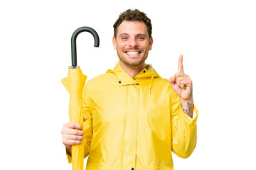 Poster - Brazilian man with rainproof coat and umbrella over isolated chroma key background pointing up a great idea