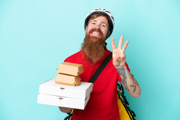 Wall Mural - Delivery man holding pizzas and burgers isolated on blue background happy and counting three with fingers