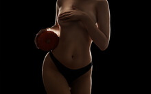 Sexy Slim Woman Holds A Pumpkin And Covers Her Chest With Her Hand On A Black Background.
