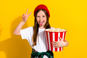 Poster - Photo portrait of charming schoolgirl showing v-sign popcorn stick tongue wear trendy white garment isolated on yellow color background