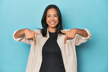Filipina Young Woman On Blue Studio Points Down With Fingers, Positive Feeling.