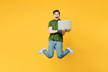 Wall Mural - Full body surprised young shocked happy IT man wears green t-shirt casual clothes jump high hold use work on laptop pc computer isolated on plain yellow background studio portrait. Lifestyle concept.