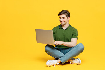 Full body young programmer smart happy IT man he wears green t-shirt casual clothes sitting hold use work on laptop pc computer isolated on plain yellow background studio portrait. Lifestyle concept.