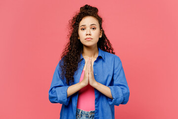 Wall Mural - Young woman of African American ethnicity she wear blue shirt casual clothes hold hands folded in prayer gesture, begging about something isolated on plain pastel pink background. Lifestyle concept.