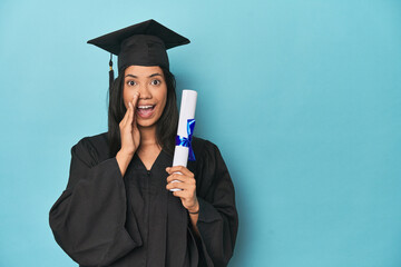 Wall Mural - Filipina graduate with diploma on blue studio is saying a secret hot braking news and looking aside