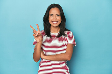 Filipina young woman on blue studio showing number two with fingers.
