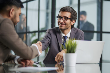 Wall Mural - Business colleagues sitting at a table during a meeting with two male executives shaking hands