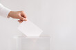 Woman putting her vote into ballot box on light grey background, closeup. Space for text