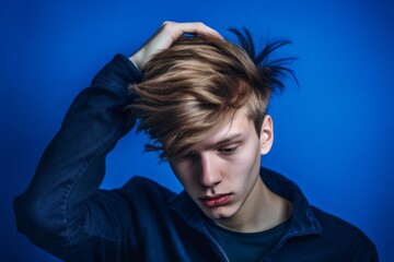 Poster - Close-up portrait photography of a beautiful boy in his 20s scratching head in gesture of confusion against a royal blue background. With generative AI technology