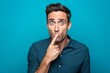 © Markus Schröder - Lifestyle portrait photography of a satisfied boy in his 30s making a silence gesture by putting the index finger on the lips against a turquoise blue background. With generative AI technology