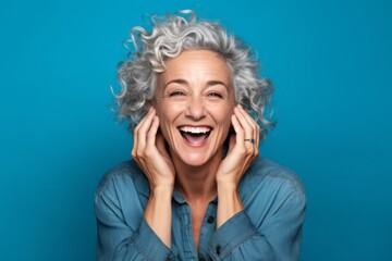 Canvas Print - Headshot portrait photography of a grinning mature woman covering his ears against a turquoise blue background. With generative AI technology