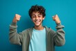 © Markus Schröder - Close-up portrait photography of a joyful boy in his 20s raising both thumbs up against a turquoise blue background. With generative AI technology