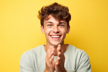 Wall Mural - Close-up portrait photography of a grinning boy in his 20s joining palms in a gesture of gratitude against a pastel yellow background. With generative AI technology