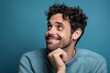 © Markus Schröder - Close-up portrait photography of a joyful boy in his 30s putting the hand on the chin as if thinking against a soft blue background. With generative AI technology