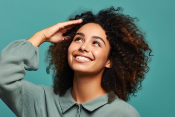 Wall Mural - Close-up portrait photography of a happy girl in her 20s putting the hand on the forehead to look for someone in the distance against a pastel green background. With generative AI technology