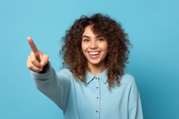 Wall Mural - Close-up portrait photography of a happy girl in her 20s pointing with two hands and fingers to the side against a sky-blue background. With generative AI technology