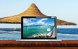 Search hotels website on laptop computer screen, a straw beach umbrella and tropical beach on background. Online booking concept.