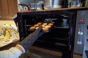 Wall Mural - Unrecognizable person taking cupcakes from oven