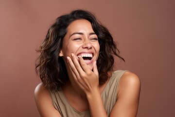 Wall Mural - Headshot portrait photography of a satisfied girl in her 30s placing the hand over the mouth in a laughter gesture against a warm taupe background. With generative AI technology