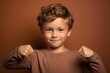 © Markus Schröder - Medium shot portrait photography of a satisfied kid male making a i'm strong gesture showing muscles against a copper brown background. With generative AI technology