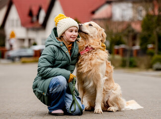 Sticker - Preteen child girl sitting with golden retriever dog at autumn city street wearing hat and warm jacket. Pretty kid hugging purebred pet doggy labrador outdoors