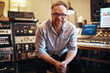 © Flamingo Images - Music producer smiling while sitting in his recording studio
