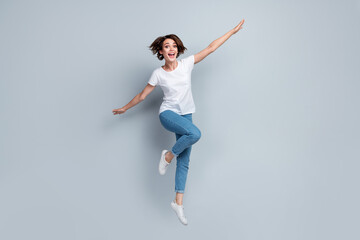 Full size photo of overjoyed nice girl jumping arms wings flying empty space isolated on grey color background