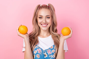 Sticker - Portrait of toothy beaming pretty girl with ponytails wear t-shirt under dress arms hold two oranges isolated on pink color background