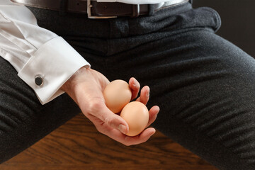 Two eggs in a man's hand. Pair of eggs in a male palm hand. Concept of male infertility, testicular cancer and impotence. Hand with two hen's eggs. Shallow depth of field